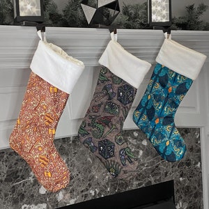 May include: Three Christmas stockings with different patterns. The stocking on the left has a red and gold pattern. The stocking in the middle has a blue, green, and purple pattern with a dragon design. The stocking on the right has a blue and gold pattern with a star design.