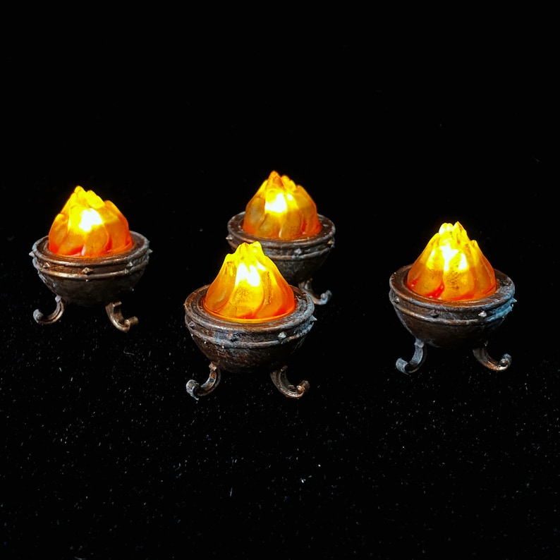 May include: Four small, decorative metal braziers with orange flame-shaped lights inside. The braziers have a dark brown finish and three legs.