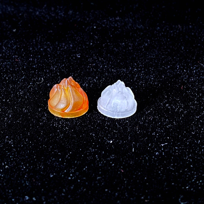 May include: Two small, decorative, ceramic figurines in the shape of a flame. One is orange and the other is white.