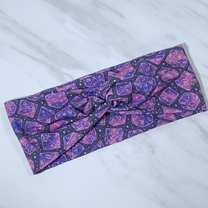 Puede incluir: Diadema morada y rosa con estampado de galaxia con dados dorados con n&uacute;meros.