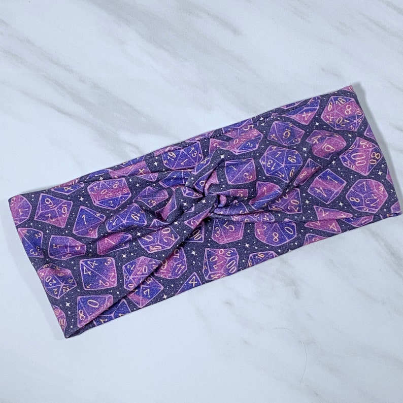 Puede incluir: Diadema morada y rosa con estampado de galaxia con dados dorados con n&uacute;meros.
