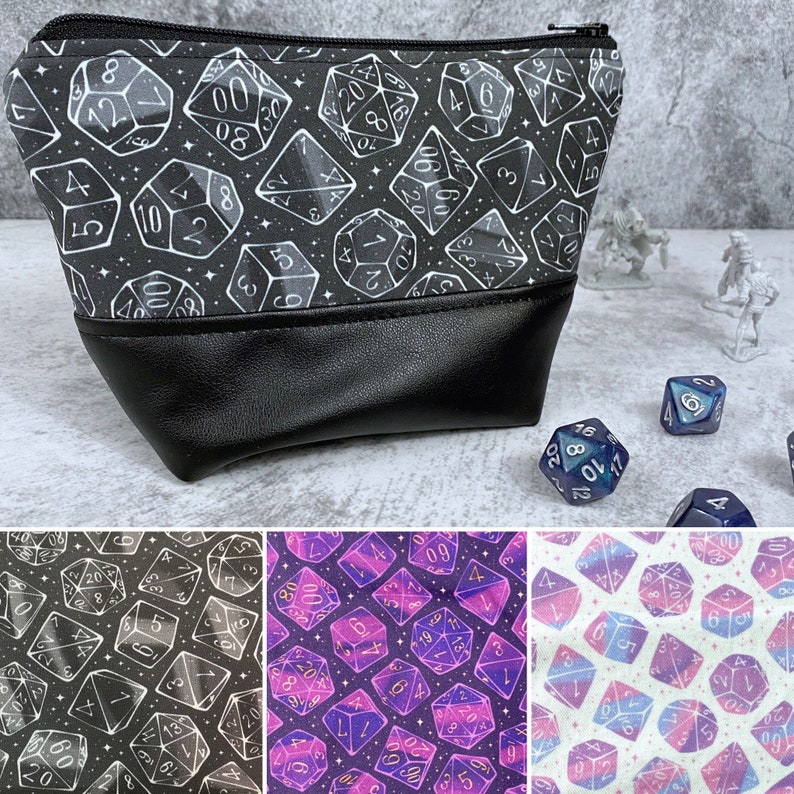 May include: A black zippered pouch with a white and silver design of dice. The pouch is made of a soft, textured fabric and has a black leather flap.