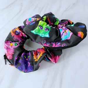 May include: Black scrunchie with a zipper closure and a colorful print of cartoon monsters and creatures.