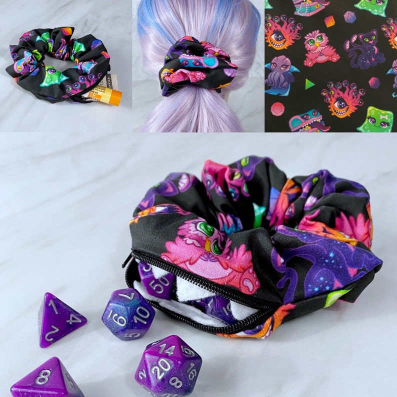 May include: A black scrunchie with a zippered pocket and a colorful print of cartoon monsters. The scrunchie is open and there are five purple dice inside. The dice are numbered 1-4, 1-10, 1-20, 1-6, and 1-8.