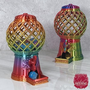 May include: Two rainbow iridescent metal gumball machines with a gold-colored wire cage. The gumball machines have a crank on the side and a tray at the bottom to dispense the gumballs. The gumball machines are filled with colorful dice.