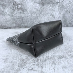 May include: A black zippered pouch with a white and gray patterned design. The pouch is made of a soft, textured fabric and has a black zipper.