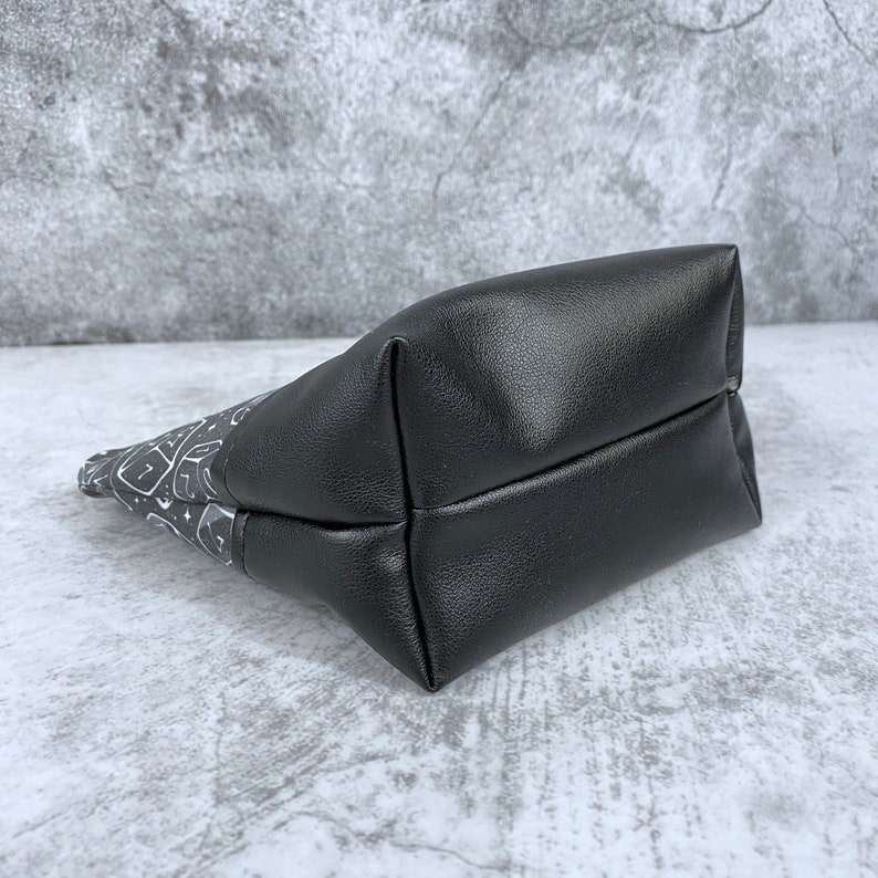 May include: A black zippered pouch with a white and gray patterned design. The pouch is made of a soft, textured fabric and has a black zipper.