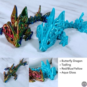 May include: Two 3D printed dragon figurines. One is iridescent red, blue, and yellow, and the other is aqua blue. Both have intricate details and a glossy finish.