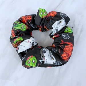 May include: Black scrunchie with a Halloween-themed print featuring ghosts, zombies, dice, and other spooky imagery.