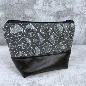 May include: A black zippered pouch with a white and gray dice pattern. The pouch has a black faux leather bottom.