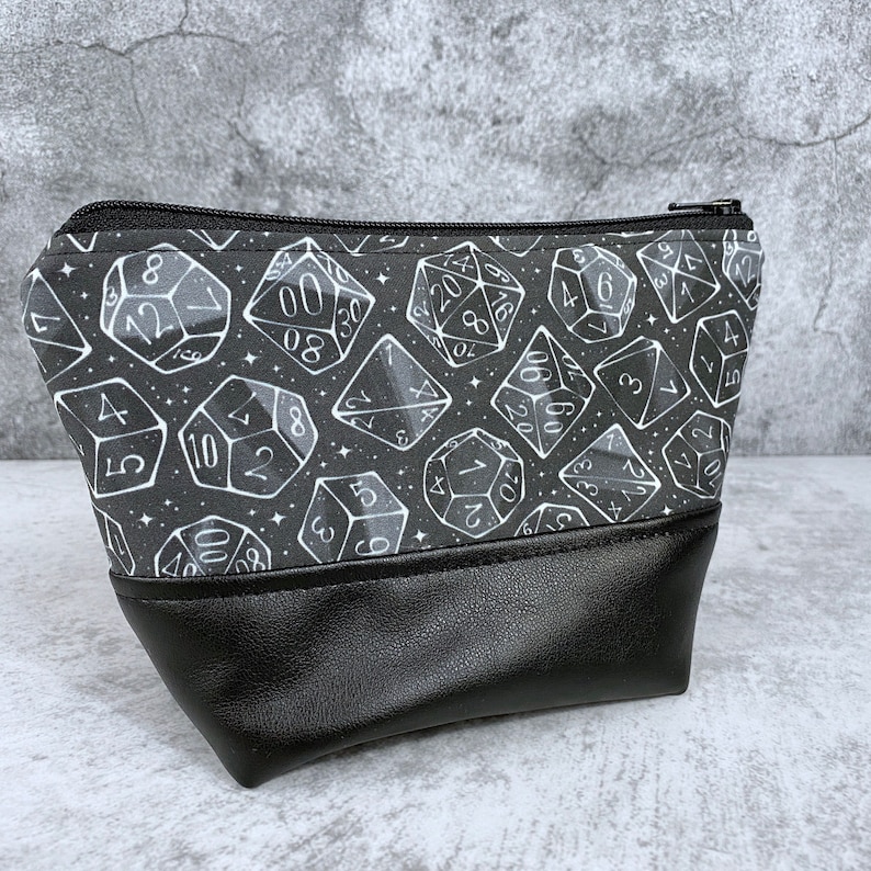 May include: A black zippered pouch with a white and gray dice pattern. The pouch has a black faux leather bottom.