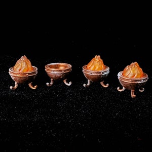 May include: Four miniature metal fire pits with orange flames. The fire pits have three legs and are made of a dark brown metal.