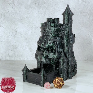 Könnte beinhalten: Ein schwarz-grüner 3D-gedruckter Schädel-Würfeltower mit einem Schloss auf der Oberseite. Der Turm hat einen Schlitz, aus dem die Würfel aus dem Mund des Schädels rollen können. Zwei Würfel sind auf einer weißen Oberfläche vor dem Turm zu sehen.