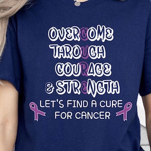 May include: Navy blue t-shirt with white and purple text: "Overcome Through Courage & Strength" and "Let's Find a Cure for Cancer" with purple ribbon graphics. The shirt is a crew neck style.