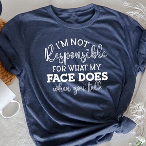 Könnte beinhalten: Ein marineblaues T-Shirt mit dem Aufdruck "Ich bin nicht verantwortlich für das, was mein Gesicht tut, wenn du sprichst" in weiß.