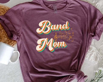 Może przedstawiać: Koszulka w kolorze brązowym z nadrukiem "Band Mom" w stylu retro z nutami muzycznymi.