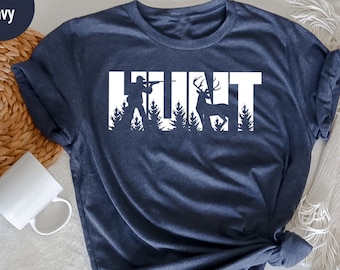 May include: A heather navy blue t-shirt with a white graphic of a hunter and deer with the word "HUNT" spelled out using the silhouettes of the hunter, deer, and trees.