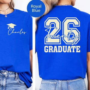 May include: Royal blue t-shirt with a graduation cap and the name "Charles" printed on the front. The back of the shirt features the number "26", the word "Twenty", and the word "GRADUATE" in a cream color.