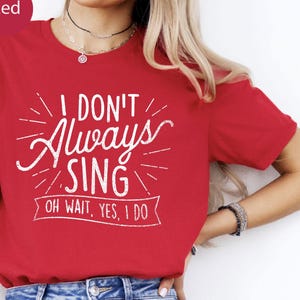 May include: A red short-sleeved t-shirt featuring white screen-printed text that reads I DON'T Always SING OH WAIT, YES, I DO. The design includes decorative lines radiating from the text and a banner graphic underneath the final phrase.