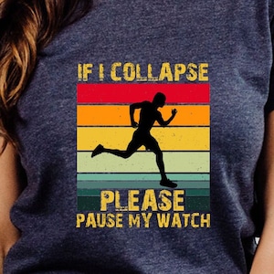 May include: A navy blue t-shirt with a vintage-style graphic that says "If I Collapse Please Pause My Watch". The graphic features a silhouette of a runner against a colorful sunset background.