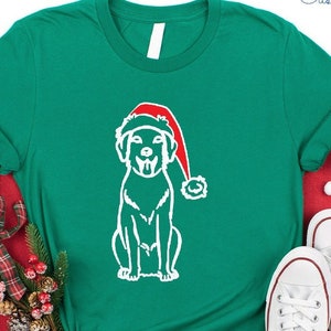 May include: Kelly green t-shirt featuring a white graphic of a dog wearing a Santa hat. The shirt is paired with white sneakers. The text "NFINITI Custom Shirts" is visible in the upper right corner. The shirt is displayed on a red surface with Christmas decorations.