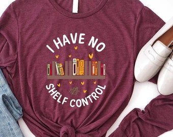 May include: A maroon long-sleeve t-shirt with the text "I have no shelf control" in white. The text is surrounded by a circle of small hearts and a graphic of a bookshelf with colorful books.