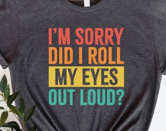 May include: A dark heather grey t-shirt with the text "I'M SORRY DID I ROLL MY EYES OUT LOUD?" in a retro rainbow color scheme.