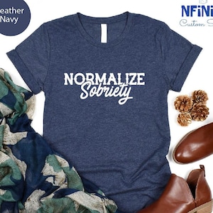 Może przedstawiać: Koszulka w kolorze granatowym z melanżem, z nadrukiem "Normalizuj trzeźwość" w kolorze białym na przodzie. Koszulka jest prezentowana na białym tle z szalikiem i brązowymi butami.