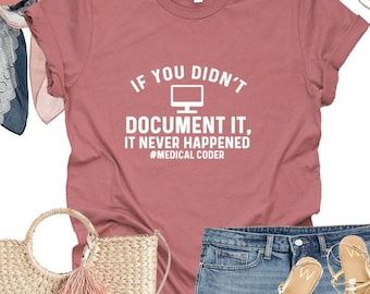 May include: A heather mauve t-shirt with the text "If you didn't document it, it never happened #medical coder" in white. The shirt is paired with denim shorts, a straw bag with a pink tassel, and white sandals.
