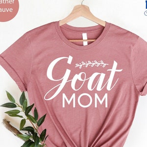 May include: Heather mauve t-shirt with the text "Goat Mom" in white lettering with a small leafy design above the word "Goat".