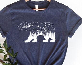 Puede incluir: Una camiseta azul marino jaspeada con un gráfico blanco de una silueta de oso con una cordillera y estrellas en su interior. El texto "NFINITI Custom Shirts" está en la esquina superior derecha de la imagen.