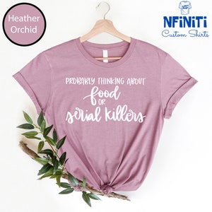 May include: A heather orchid t-shirt with the text "Probably thinking about food or serial killers" in white lettering.