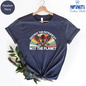 May include: A navy blue t-shirt with a vintage-style graphic that says "Destroy the Patriarchy Not the Planet". The graphic features a stylized uterus with flowers and a rainbow.