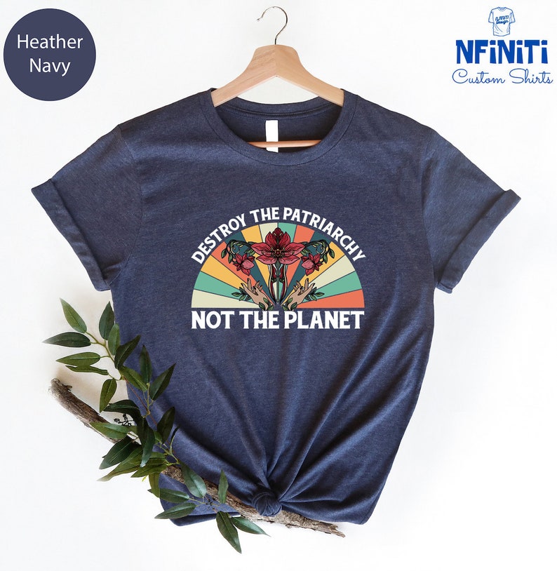 May include: A navy blue t-shirt with a vintage-style graphic that says "Destroy the Patriarchy Not the Planet". The graphic features a stylized uterus with flowers and a rainbow.