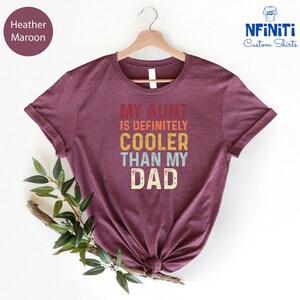 May include: Heather maroon t-shirt with the text "My Aunt is Definitely Cooler Than My Dad" in a retro rainbow color scheme.