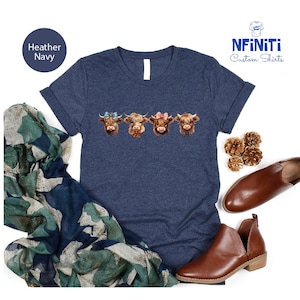 Puede incluir: Camiseta azul marino jaspeada con un gr&aacute;fico de cuatro vacas de las tierras altas con lazos. Las vacas son marrones con marcas blancas y tienen lazos de diferentes colores. El texto "NFINITI Custom Shirts" est&aacute; en la esquina superior derecha de la imagen.