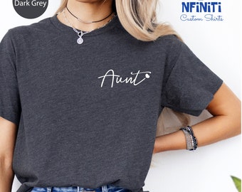 May include: Heather dark grey t-shirt with the word "Aunt" in white script on the front. The shirt is a crew neck style. The brand name "NFiniTi Custom Shirts" is in the upper right corner.