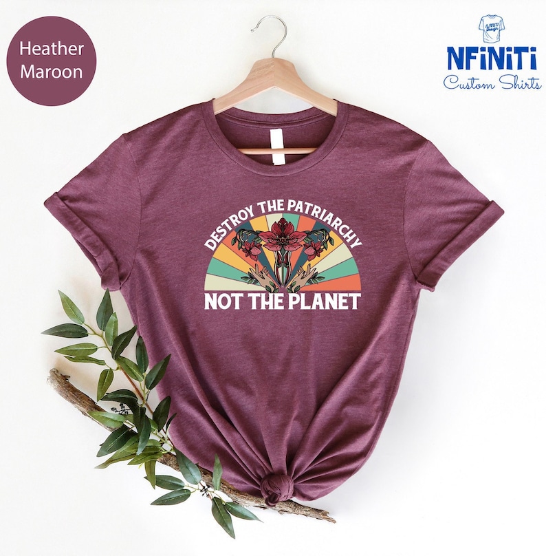 May include: Heather maroon t-shirt with a vintage-style graphic that says "Destroy the Patriarchy Not the Planet". The graphic features a stylized uterus with flowers and a rainbow.