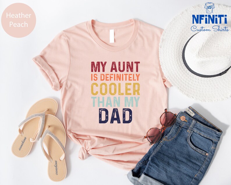 May include: A pink t-shirt with the text "My Aunt is Definitely Cooler Than My Dad" in a retro rainbow font.