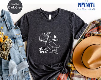 May include: A dark heather grey t-shirt with a white graphic of a duck eating a slice of bread. The text on the shirt reads "is this gluten free?"