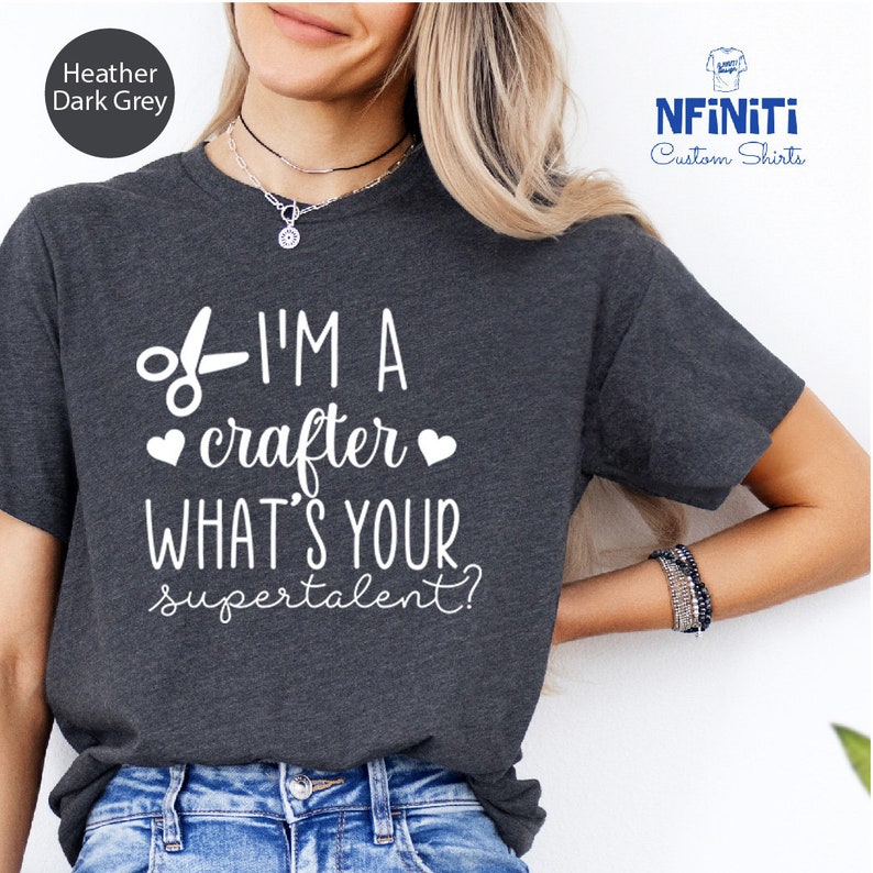 Op de afbeelding: Een donkergrijs t-shirt met de tekst "I'M A crafter WHAT'S YOUR supertalent?" in wit gedrukt. De tekst wordt vergezeld door een schaar en twee harten.