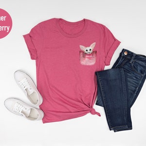 May include: Heather raspberry t-shirt with a pocket featuring a watercolor illustration of a fox. The shirt is paired with dark blue jeans and white trainers. The text "NFINTI Custom Shirts" is visible.