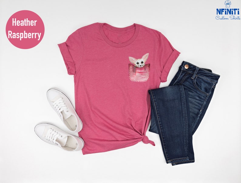 May include: Heather raspberry t-shirt with a pocket featuring a watercolor illustration of a fox. The shirt is paired with dark blue jeans and white trainers. The text "NFINTI Custom Shirts" is visible.
