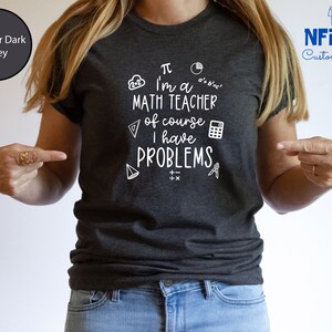 May include: Heather dark grey t-shirt with a white graphic that says "&pi; I'm a MATH TEACHER of course I have PROBLEMS". The graphic includes math symbols like a pie chart, a calculator, a compass, and a triangle.