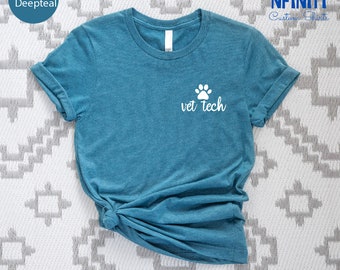 May include: Heather deep teal t-shirt with a white paw print and the words "vet tech". The shirt is made of a soft material and has rolled-up sleeves. The shirt is displayed on a patterned surface.