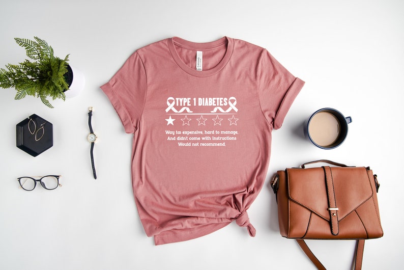 K&ouml;nnte beinhalten: Ein pinkfarbenes T-Shirt mit einer wei&szlig;en Grafik, auf der "TYPE 1 DIABETES" steht, mit einer Bewertung von 1 von 5 Sternen und dem Text "Way too expensive, hard to manage, And didn't come with instructions. Would not recommend."