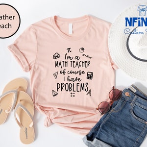 May include: A pink t-shirt with a black graphic that says "I'm a math teacher of course I have problems". The graphic includes math symbols like pi, a calculator, and a protractor.