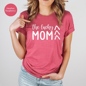 May include: Heather raspberry-colored t-shirt with the text "the lucky MOM" in white. The shirt has short sleeves and a crew neck. The text is centered on the front of the shirt. The shirt is made of a soft material.