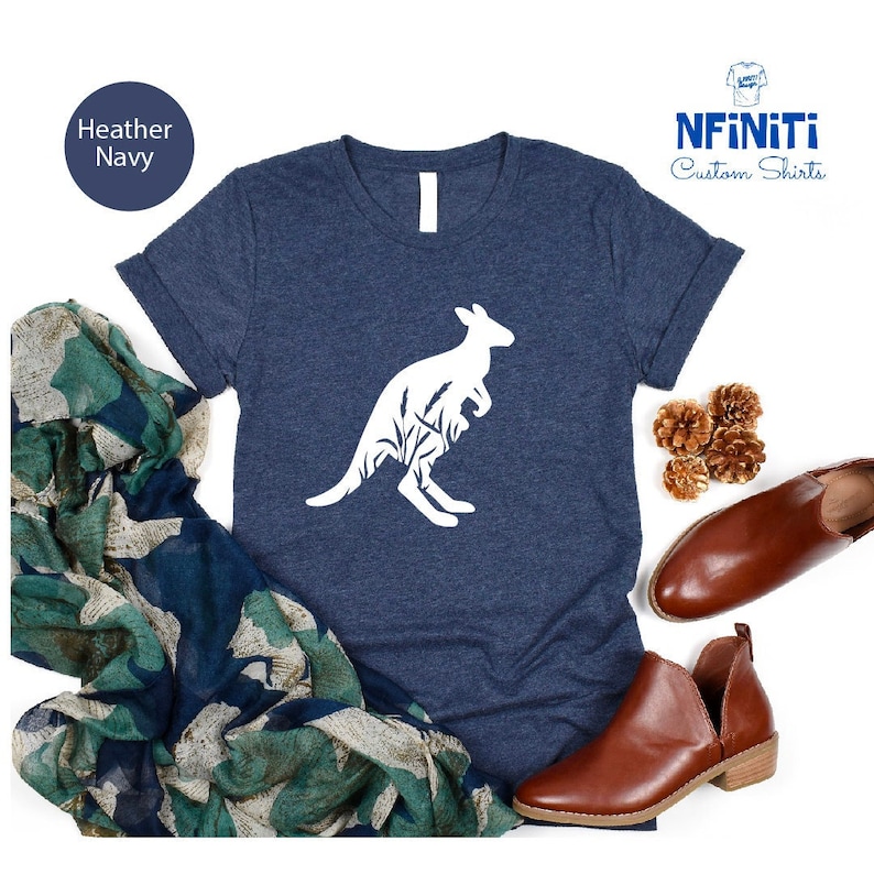 May include: A heather navy blue t-shirt with a white silhouette of a kangaroo with a joey in its pouch. The kangaroo is surrounded by a design of leaves and branches. The text "NFINITI Custom Shirts" is in the top right corner of the image.