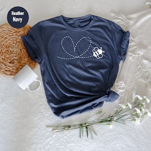 Peut inclure: Un t-shirt bleu marine chin&eacute; avec une abeille blanche volant en ligne pointill&eacute;e qui forme un c&oelig;ur.
